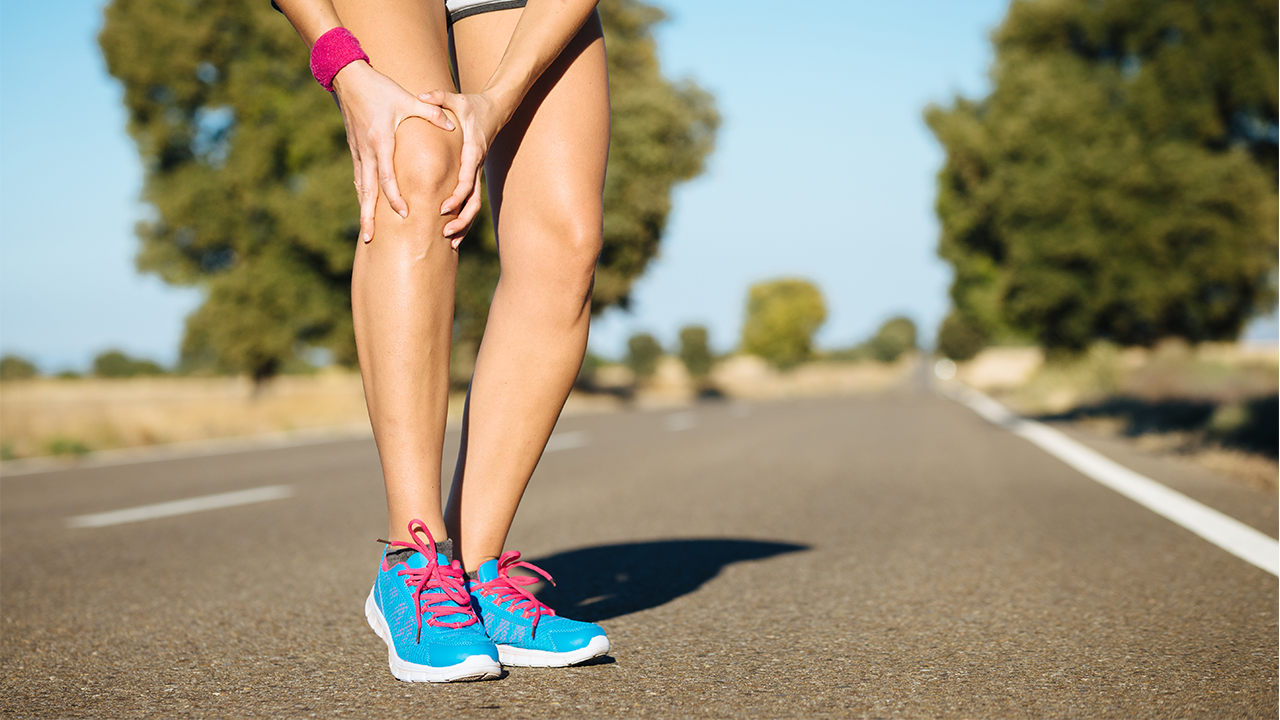 Woman outside running, she's bent over holder her knee