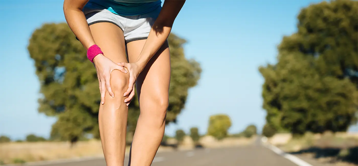 Woman outside running, she's bent over holder her knee