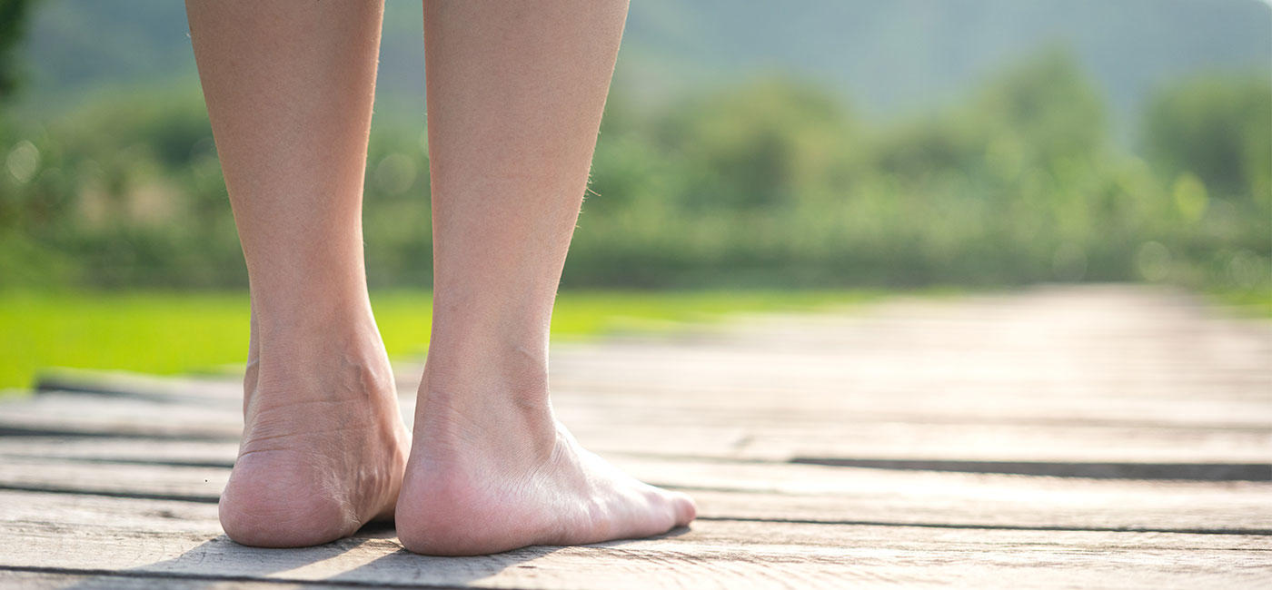 Close up of the back of a persons lower legs and feet standing on a wooden plank path, facing the horizon
