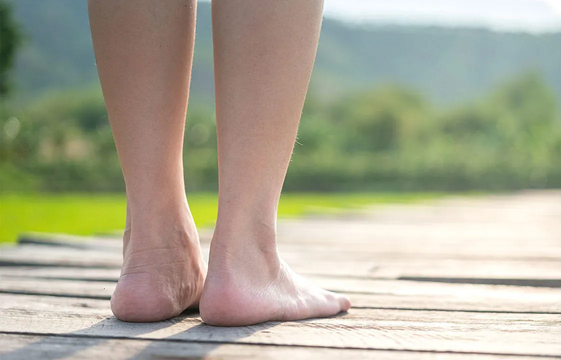 Nahaufnahme der Rückseite der Unterschenkel und Füße einer Person, die auf einem Holzbohlenweg steht, mit Blick auf den Horizont