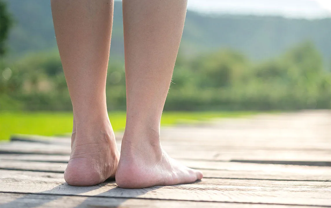 Gros plan de l'arrière des jambes et des pieds d'une personne debout sur un chemin de planches en bois, face à l'horizon.