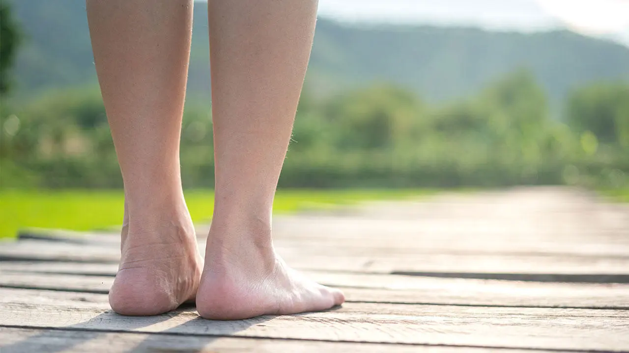 Close up of the back of a persons lower legs and feet standing on a wooden plank path, facing the horizon 
