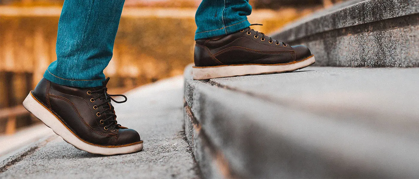 Person outside in jeans and brown shoes, walking up step.