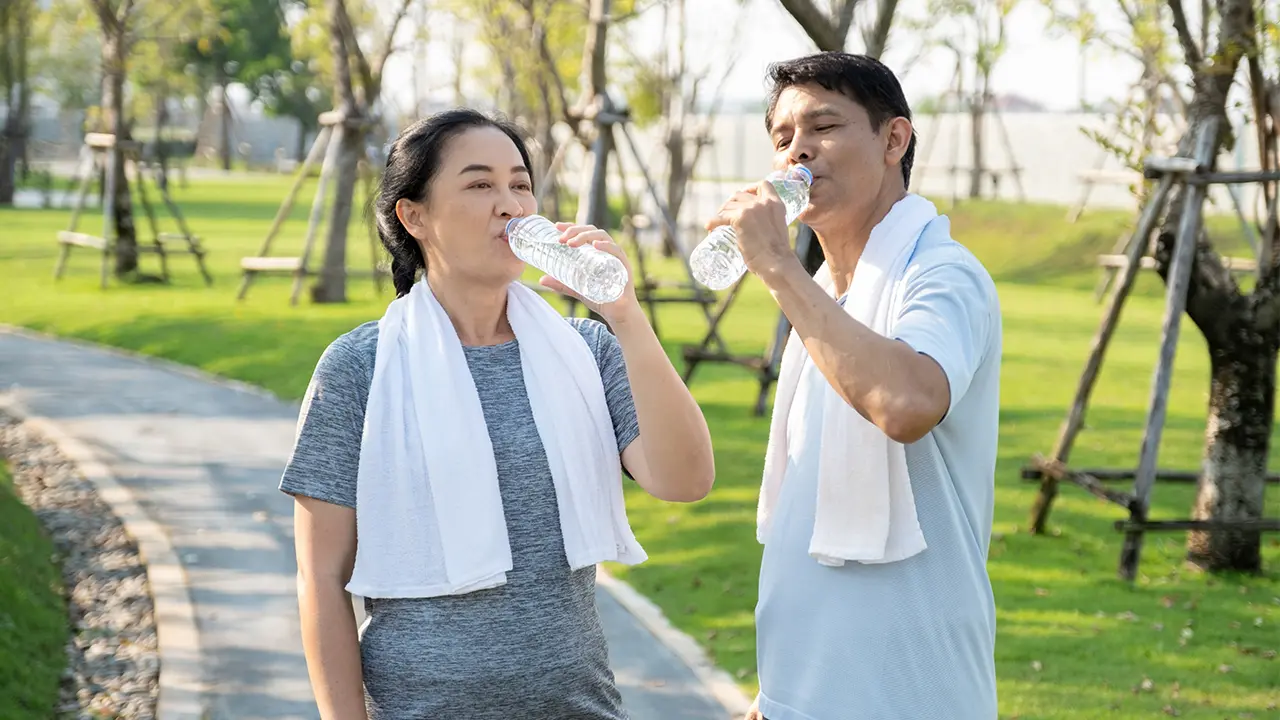 Couple out on a run in a park, they've stopped to drink water