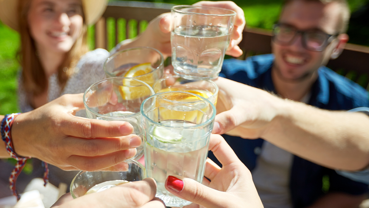 Gros plan sur un groupe de mains qui trinquent avec des verres d'eau.