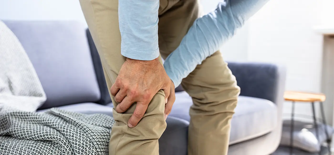 Man in his living room, bent down holding his knee