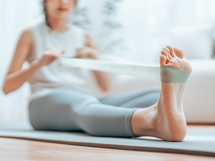 Woman sat on a yoga mat with one leg extended, using a resistant band 
