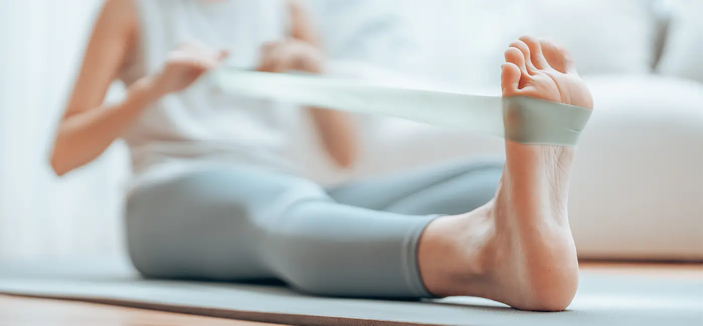 Woman sat on a yoga mat with one leg extended, using a resistant band