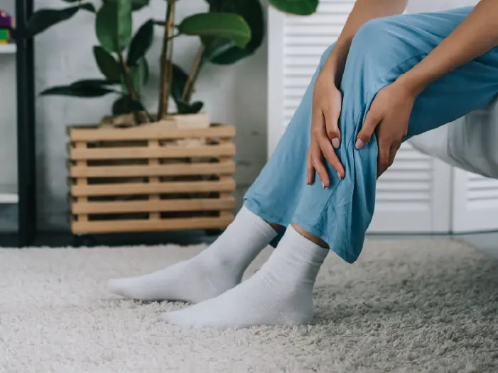 Woman on edge of bed holding leg