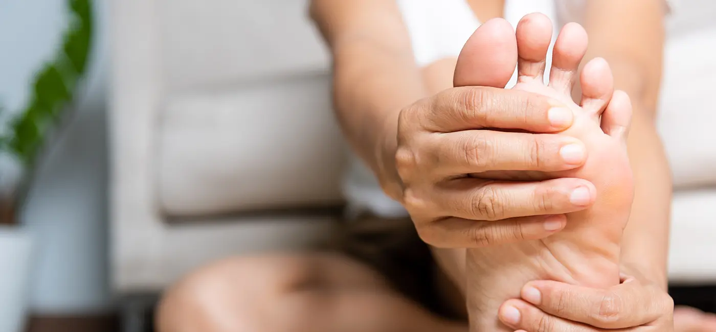 Womans foot in from of the camera, she is bent over holding the top and bottom of her foot