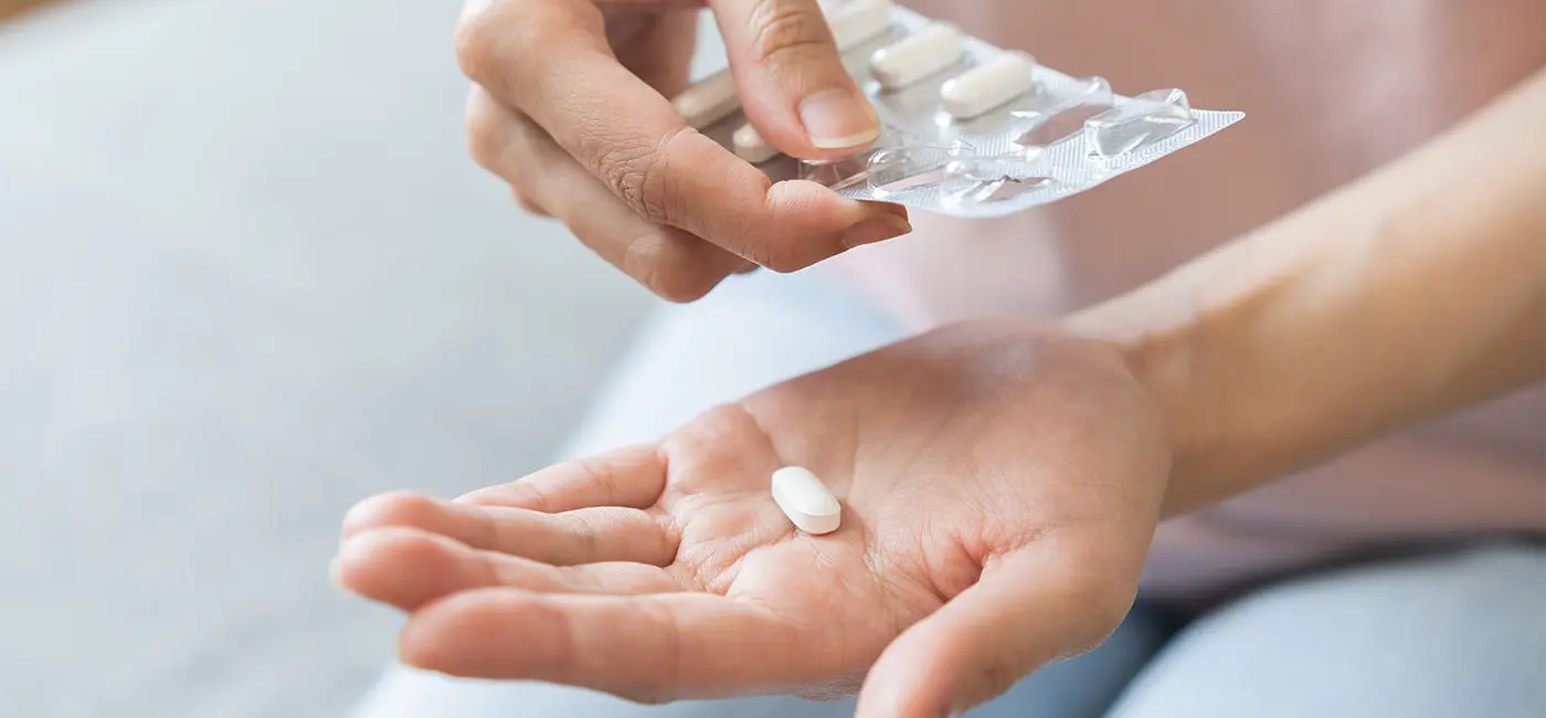 Close-up of a person opening a medical blister pack, dispensing a pill in the palm of their hand.