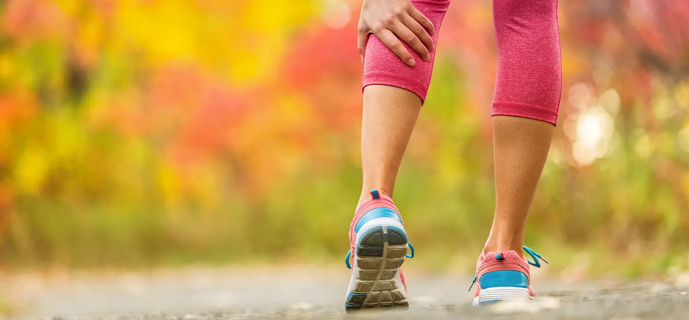 Close up of woman wearing pink leggings and trainers holding her calf muscle with her hand