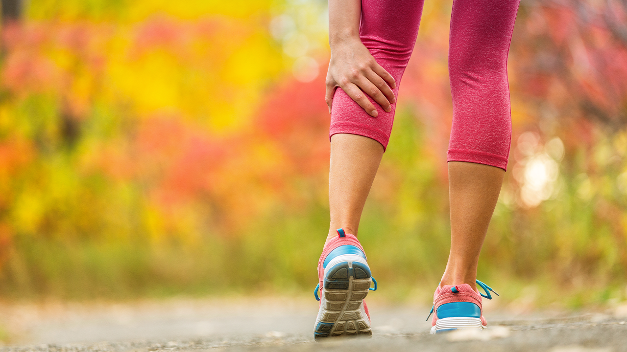 Close up of woman wearing pink leggings and trainers holding her calf muscle with her hand