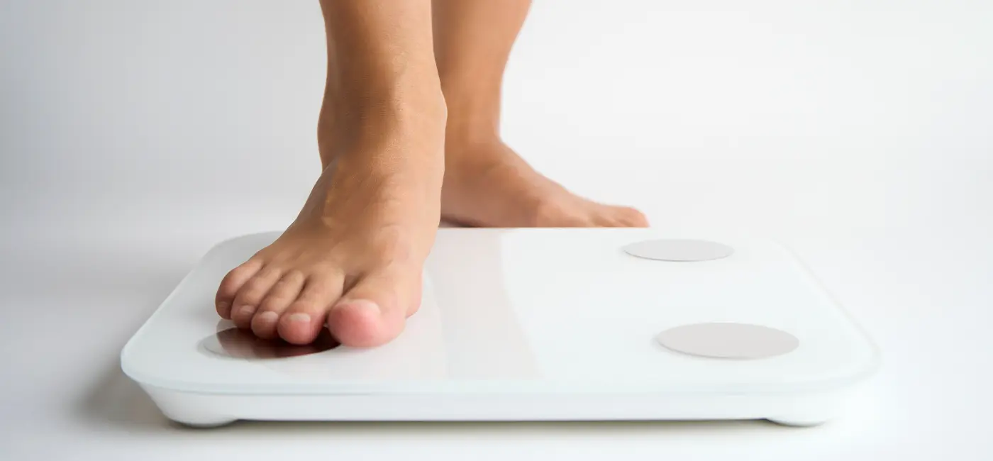 Close-up of bare feet stepping on a weighing scale. Only one foot is on the scale. 