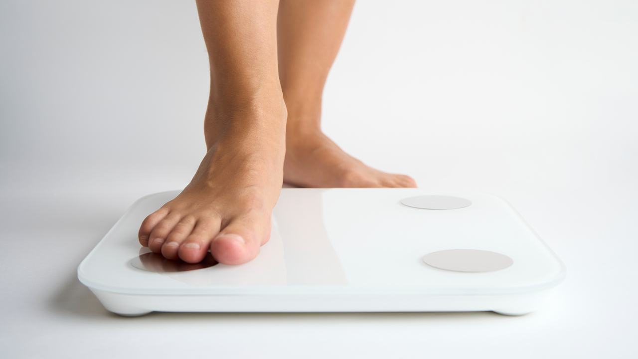 Close-up of bare feet stepping on a weighing scale. Only one foot is on the scale.