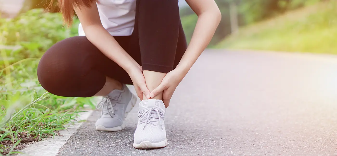Lady crouching - holding onto her right ankle on the roadside.
