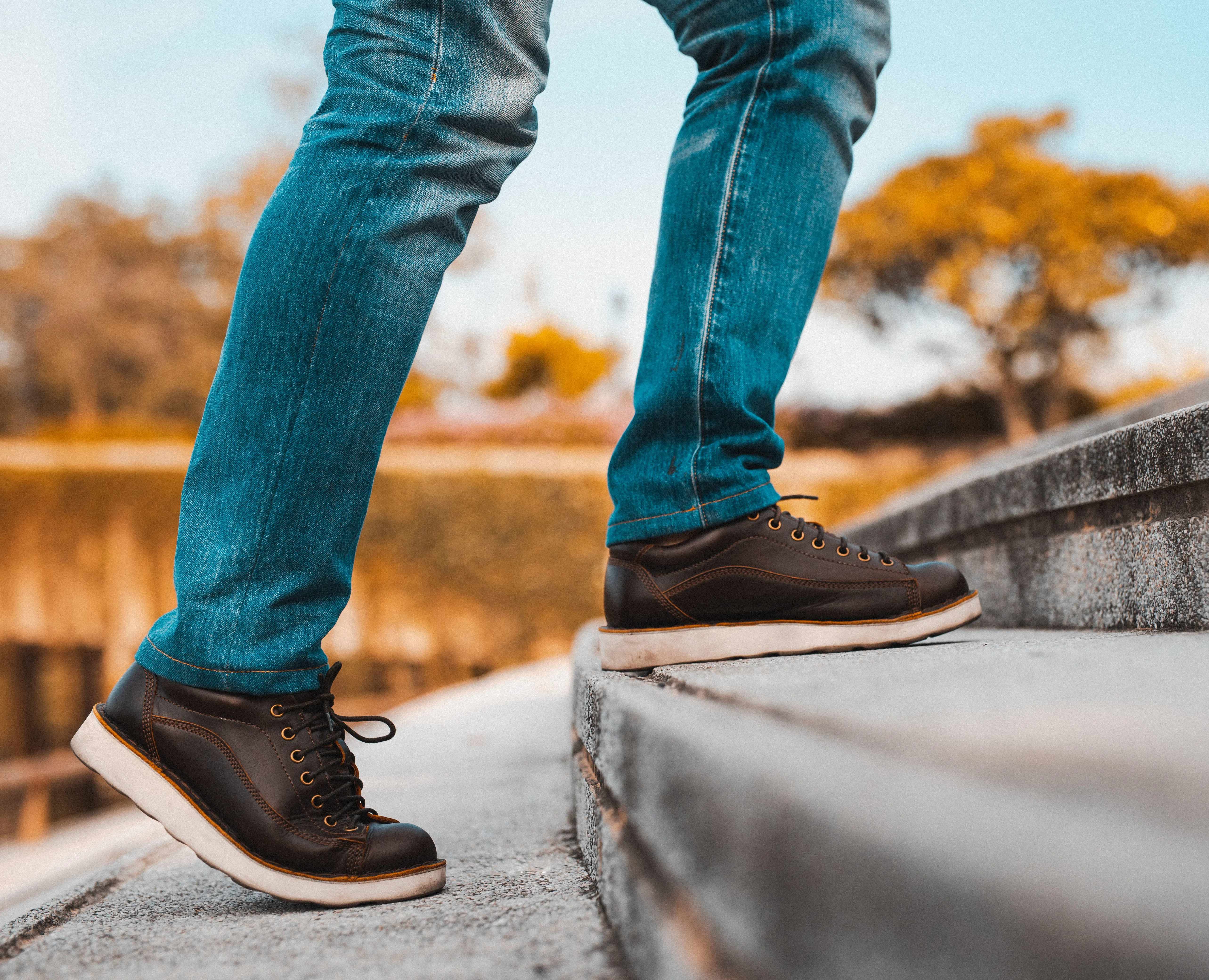 Person outside in jeans and brown shoes, walking up step.