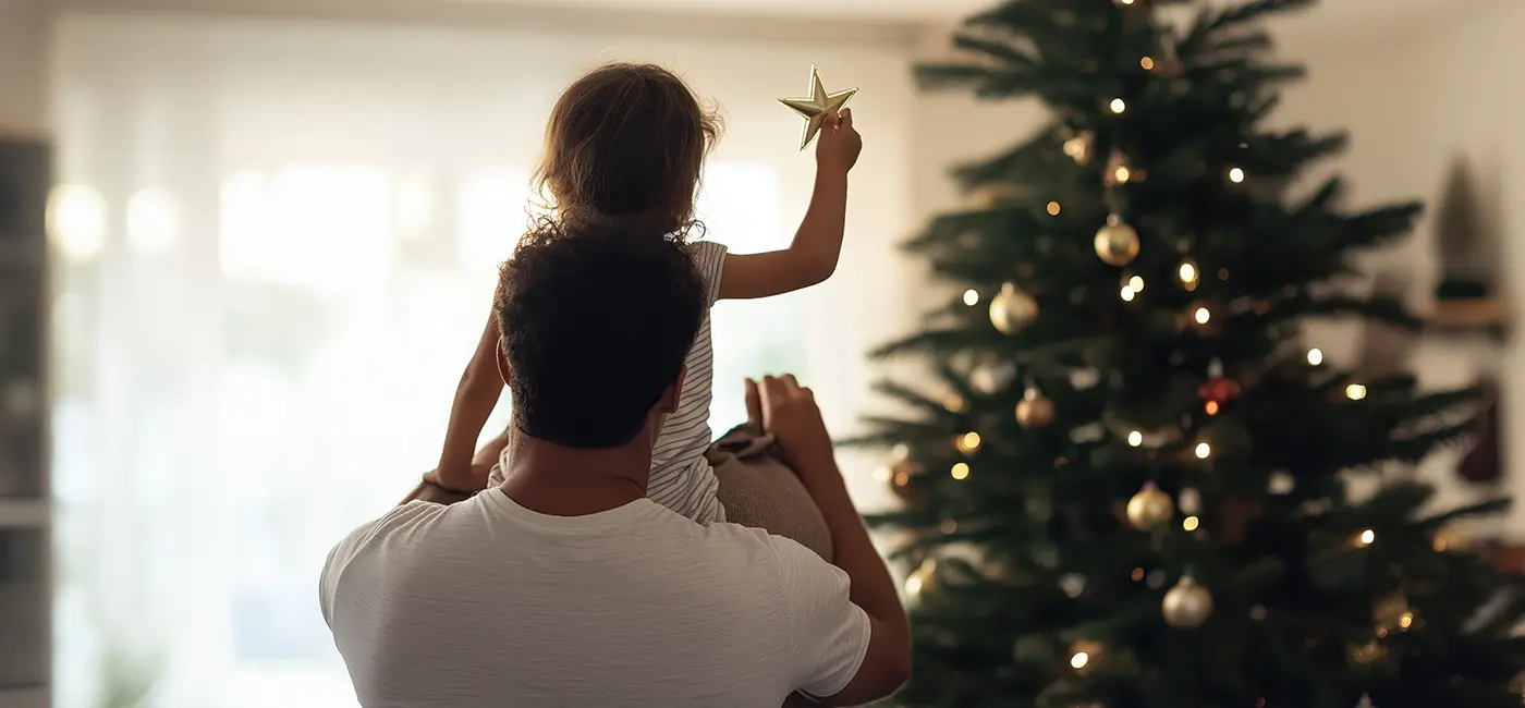Man holding child decorating a christmas tree