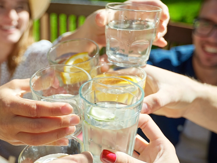 A close-up of a group of hands toasting with glasses of water. 