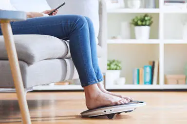 Side view image of a woman legs and feet on the coach device with her phone in her hand 